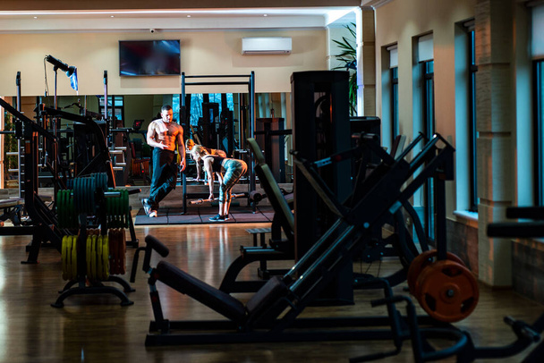 Спортивная сексуальная пара тренируется в спортзале. Личный тренер помогает женщине делать упражнения - Фото, изображение