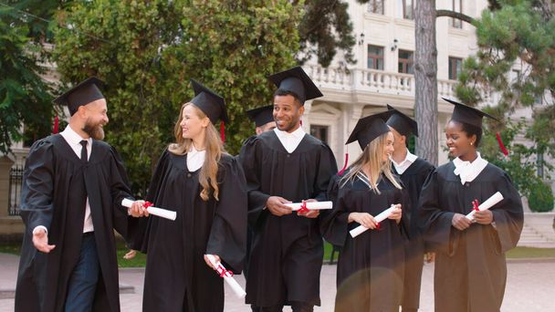 Modern college park group of multiracial graduates students after the graduation walking in front of the camera and discussing holding diplomas smiling large and feeling excited. Portrait - Foto, Imagem