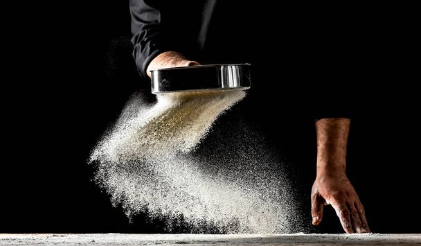 the chef sprinkles flour through a sieve, Powdery flour flying into air. chef hands with flour in a freeze motion of a cloud of flour midair. - Foto, Imagen