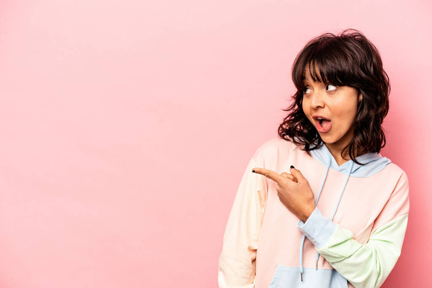 Young hispanic woman isolated on pink background points with thumb finger away, laughing and carefree. - Foto, Bild