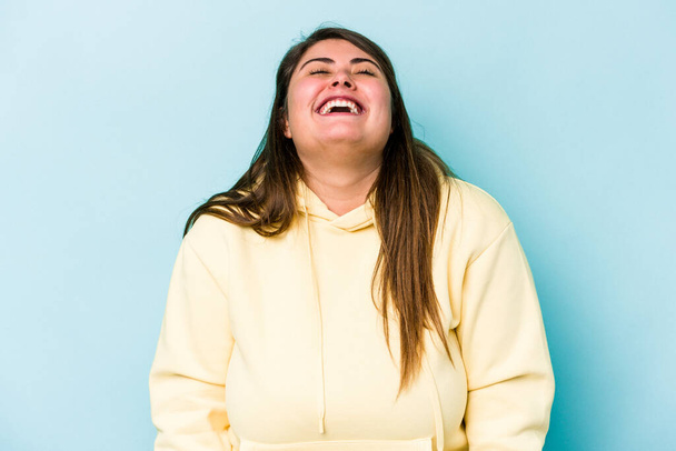 Молодая белая женщина с избыточным весом, изолированная на голубом фоне расслабленный и счастливый смех, вытянутая шея с зубами. - Фото, изображение