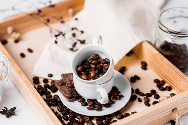 Grãos de cacau em uma xícara de café branco em uma bandeja de madeira com chocolate - Foto, Imagem