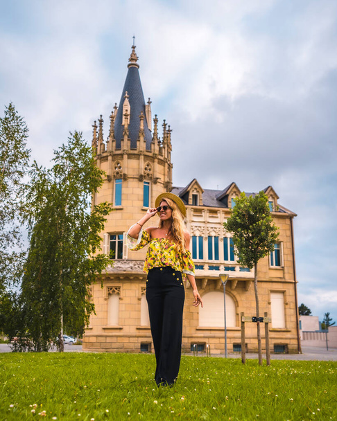 Portrait of a blonde woman in a yellow vintage outfit with a hat walking next to a castle - Photo, image
