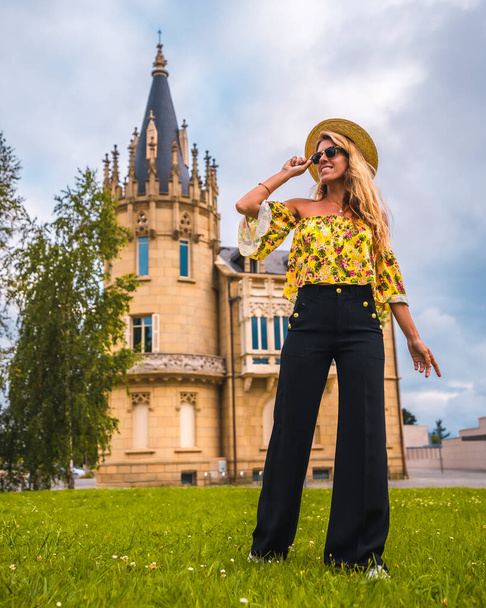 Blonde woman in a yellow vintage outfit with a hat walking next to a castle - Photo, image