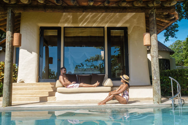 remote online werkende digitale nomade mannen en vrouwen en laptop zitten aan een zonnig turquoise water zwembad bij een prive zwembad villa, zakenman met behulp van mockup  - Foto, afbeelding