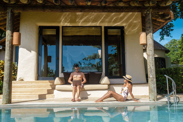 hombres y mujeres nómadas digitales de trabajo en línea remotos y portátil sentado en una piscina de agua turquesa soleada en una villa de piscina privada, hombre de negocios con maqueta  - Foto, imagen