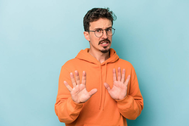 Young caucasian man isolated on blue background rejecting someone showing a gesture of disgust. - Photo, image