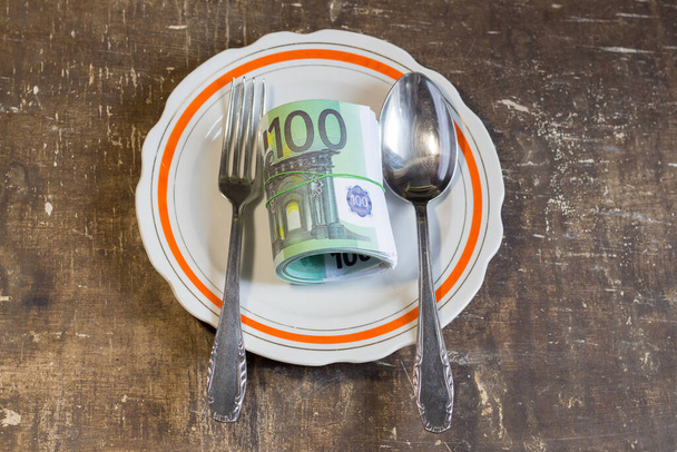 Денежные счета на тарелке на коричневом столе. Рост цен на продовольствие в связи с войной на Украине - Фото, изображение