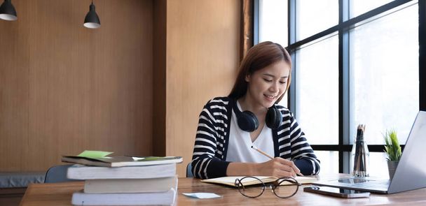 Mosolygó ázsiai egyetemista tini lány diák tanul a könyvtárban laptop könyvek csinál online kutatás tanfolyam, jegyzeteket esszé házi feladat, online oktatás e-learning koncepció - Fotó, kép