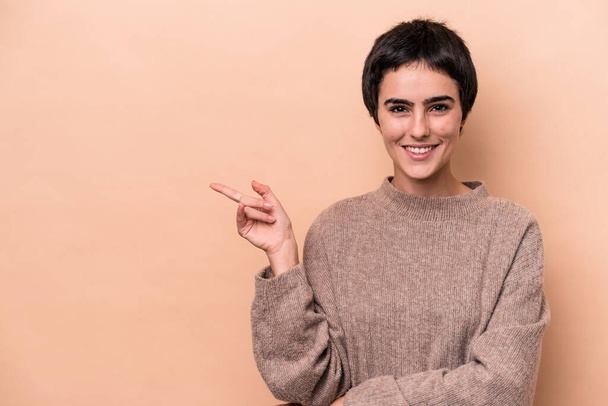 Young caucasian woman isolated on beige background smiling cheerfully pointing with forefinger away. - Photo, Image