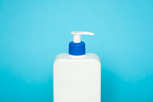 Large white cosmetic plastic bottle with pump dispenser pump and blue cap on blue background. Liquid container for gel, lotion, cream, shampoo, bath foam - Foto, Imagem