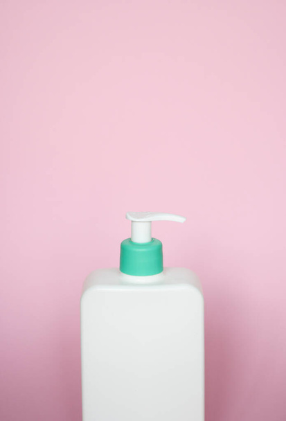 Large white cosmetic plastic bottle with pump dispenser pump and green cap on pink background. Liquid container for gel, lotion, cream, shampoo, bath foam - Photo, Image