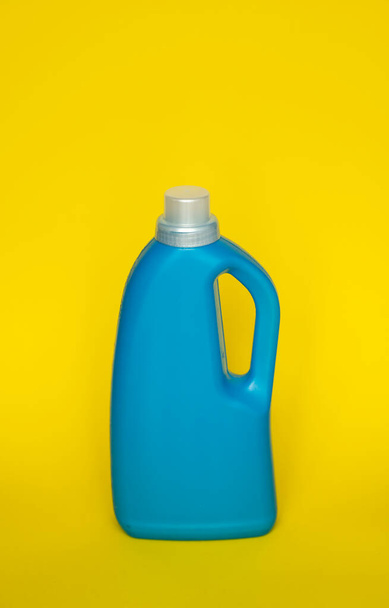 Blue plastic bottle stands on yellow background. Conditioner or liquid powder for washing. Capacity with space for copying. Layout for logo application - Foto, Bild