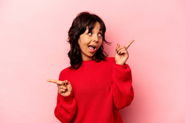 Young hispanic woman isolated on pink background pointing to different copy spaces, choosing one of them, showing with finger. - Foto, imagen