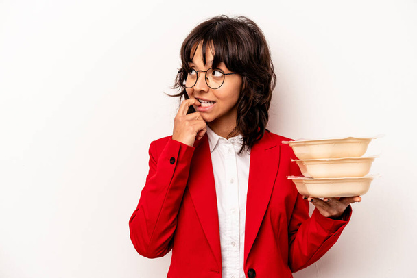 Young business hispanic woman holding tupperware isolated on white background relaxed thinking about something looking at a copy space. - Fotó, kép