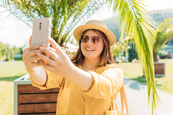 Mujer feliz en sombrero de paja tomar una selfie en vacaciones en una isla tropical, palmeras en el fondo. Viajero femenino en solitario. Concepto de verano. - Foto, imagen
