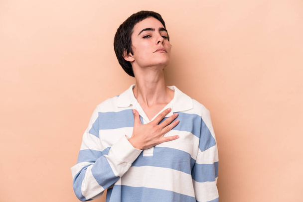 Young caucasian woman isolated on beige background taking an oath, putting hand on chest. - Photo, Image