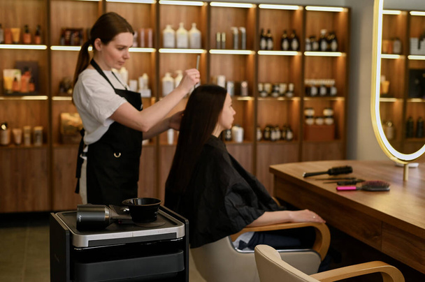 Um cabeleireiro feminino faz styling cabelo para a bela jovem mulher branca em um salão de beleza - Foto, Imagem