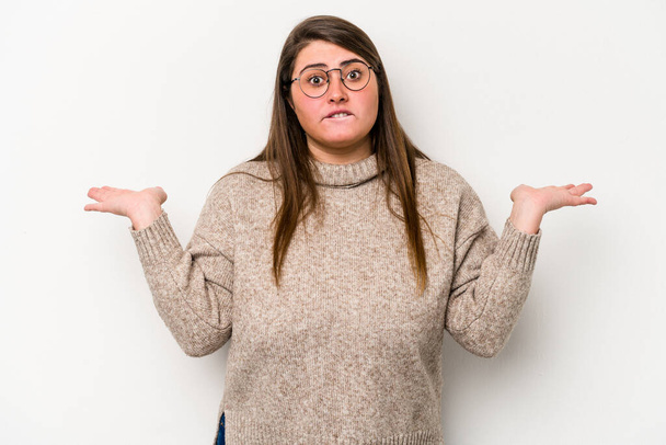 Young caucasian overweight woman isolated on white background confused and doubtful shrugging shoulders to hold a copy space. - Photo, Image