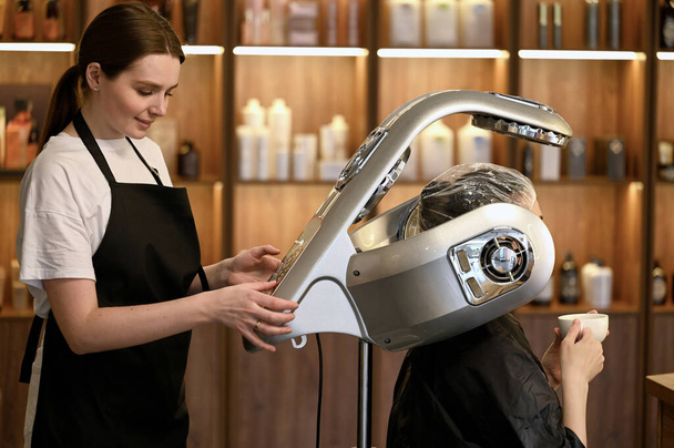 young woman under hooded dryer machine in hair salon - Foto, Imagem