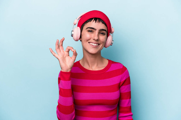 Молода біла жінка слухає музику ізольовано на фоні веселий і впевнений, показуючи ок жест
. - Фото, зображення