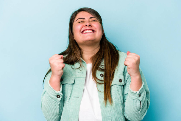 Young caucasian overweight woman isolated on blue background celebrating a victory, passion and enthusiasm, happy expression. - Photo, Image