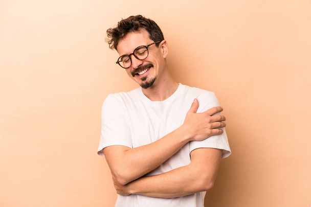 Young caucasian man isolated on beige background laughing and having fun. - 写真・画像