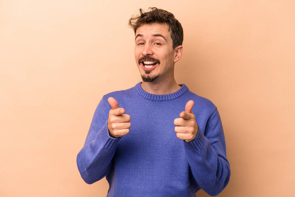 Young caucasian man isolated on beige background pointing to front with fingers. - Foto, immagini