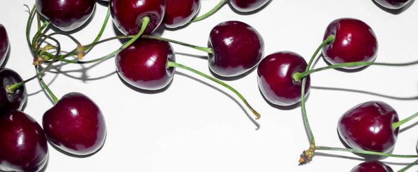Bright cherries on a white background. Clear shadows and lines. The contrast of burgundy on a white background. Contrasting photo of cherries on white with pronounced shadows. - Photo, Image