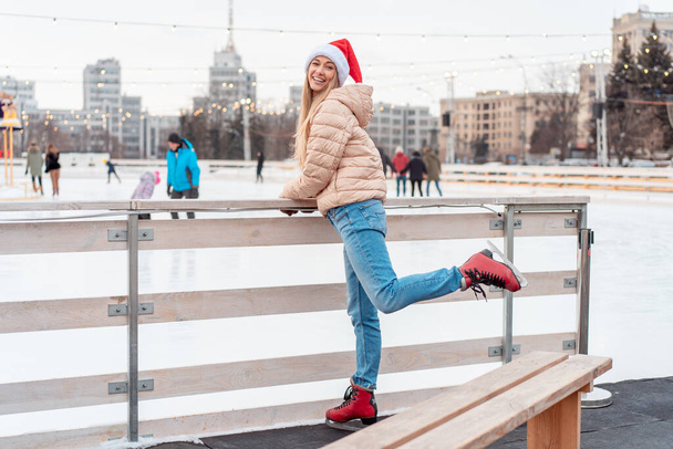 Beautiful lovely middle-aged girl blonde hair warm winter jackets knitted glove stands ice rink background Town Square. Christmas mood lifestyle Happy holiday woman walk snowy day Winter leisure - Fotografie, Obrázek