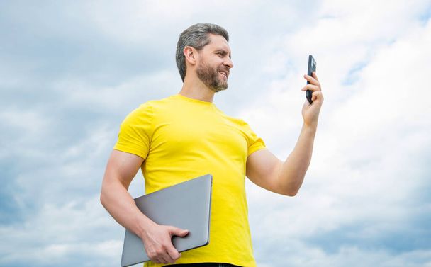 man with laptop using smartphone on sky background. - Φωτογραφία, εικόνα