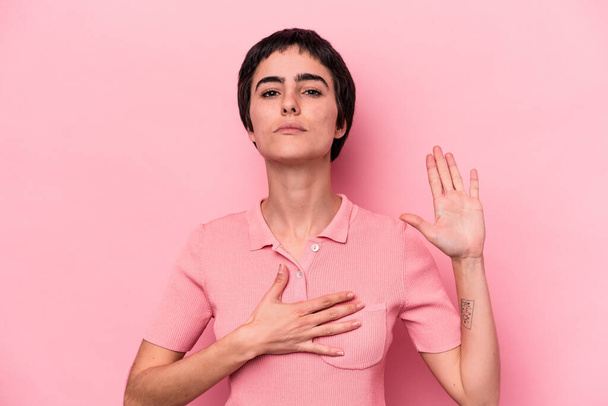 Junge kaukasische Frau isoliert auf rosa Hintergrund, die einen Eid ablegt und die Hand auf die Brust legt. - Foto, Bild