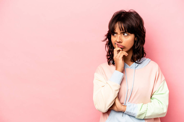 Young hispanic woman isolated on pink background looking sideways with doubtful and skeptical expression. - Photo, Image