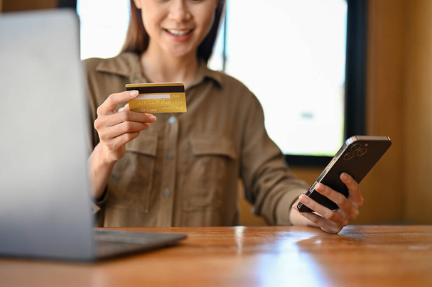 Mulher asiática jovem bonita segurando um cartão de crédito e um smartphone, usando um aplicativo de pagamento on-line internet banking no smartphone. - Foto, Imagem