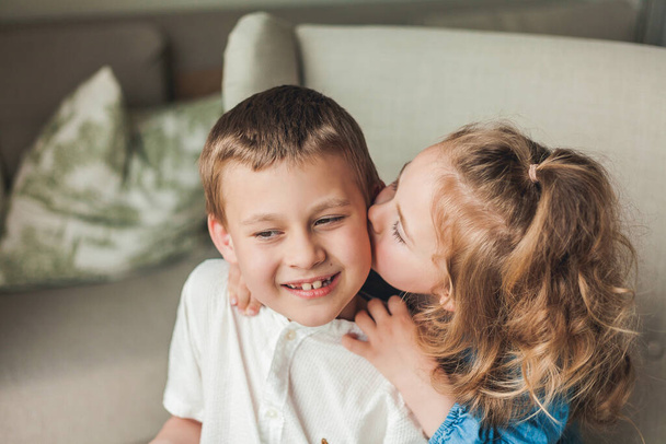 Portrait von kleinen glücklichen Kindern Bruder und Schwester sitzen in einem gemütlichen Sessel in einem hellen Haus. Familienbeziehungen. - Foto, Bild