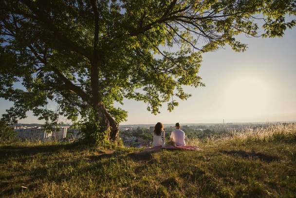 Молода пара подорожує, дивлячись на схід сонця над горою. Одруження під деревом у полі в Україні.. - Фото, зображення