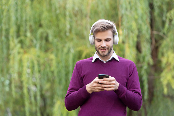 young cheerful man listen music in headphones and chating on phone outdoor. - Fotó, kép