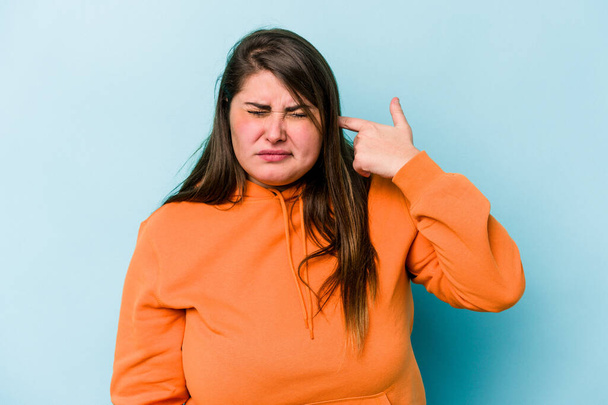 Junge kaukasische übergewichtige Frau isoliert auf blauem Hintergrund, die Ohren mit Händen bedeckt. - Foto, Bild