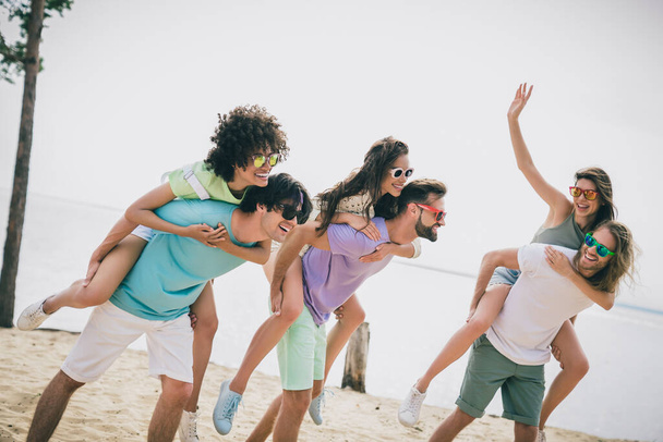 Photo of overjoyed cheerful friends piggyback ride enjoy hanging out sand beach outdoors. - Foto, Imagem