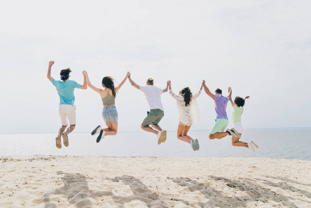Full length rear photo of excited carefree fellows hold hands jumping sea seaside outdoors. - Φωτογραφία, εικόνα