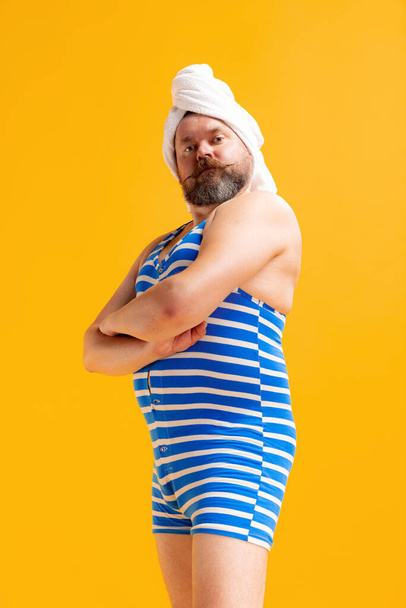 Happy morning. Comic portrait of funny fat bearded man in vintage style striped swimsuit having fun isolated on yellow background. Summer, beach, relax and fun time concept. - Zdjęcie, obraz