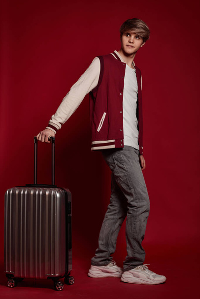 Young excited caucasian man tourist with suitcase on red background - Foto, Imagem