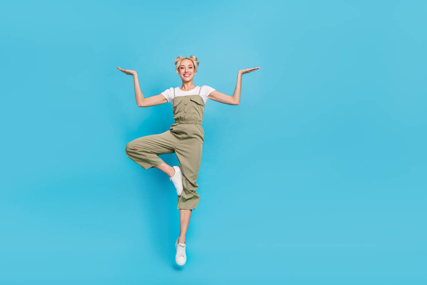 Full length photo of cute blond lady jump hold promo wear t-shirt overall shoes isolated on blue background. - Foto, immagini