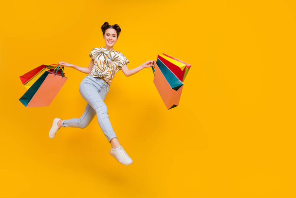 Photo of funky excited woman wear print t-shirt jumping high walking holding shoppers empty space isolated yellow color background. - Foto, Bild