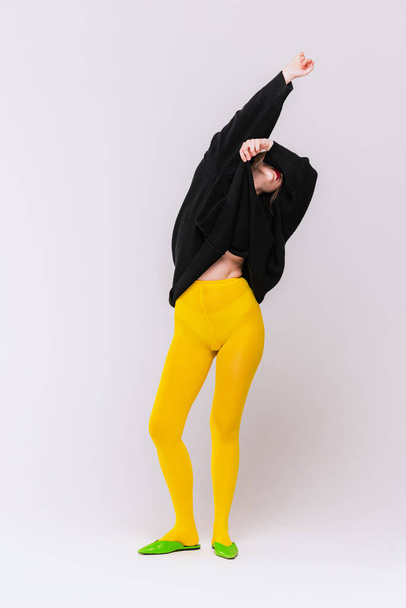 Portrait of girl in yellow tights, green vintage shoes and black jacket posing isolated over grey studio background. Concept of retro fashion, art photography, style, queer, beauty - Fotó, kép