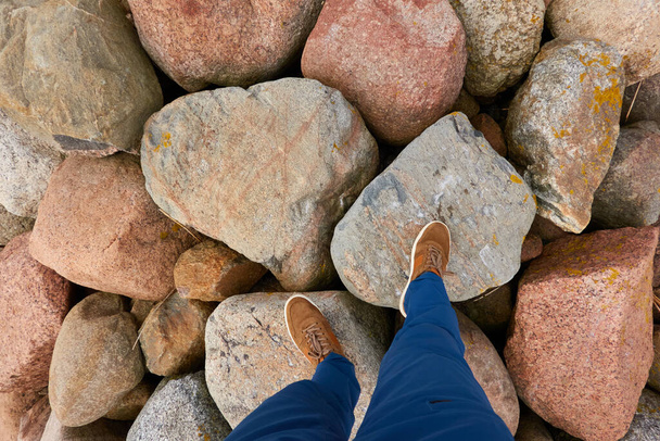 Muž v modrých džínách a hnědé boty stojící na velkých kamenech (vlnolamy). Pobřeží Baltského moře. Cestování, ekoturistika, turistika, objevování, dobrodružství, sport, zdravý životní styl témata. Zobrazení vysokého úhlu - Fotografie, Obrázek