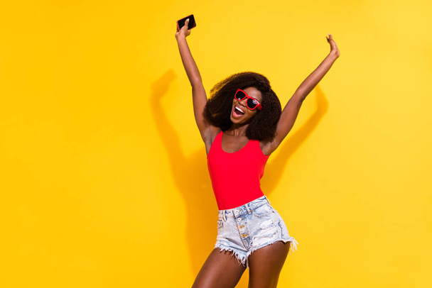 Photo of optimistic nice brunette lady hold telephone wear top shorts isolated on yellow color background. - Fotografie, Obrázek
