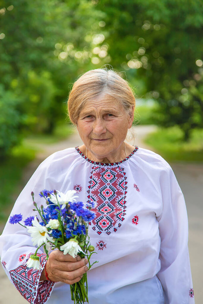 An old Ukrainian woman in an embroidered shirt with a bouquet of flowers. Selective focus. Nature. - Photo, Image