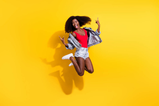 Full size photo of funky brown wavy haired afro american lady jump up make rock sign wear summer clothes isolated on yellow color background. - Fotoğraf, Görsel