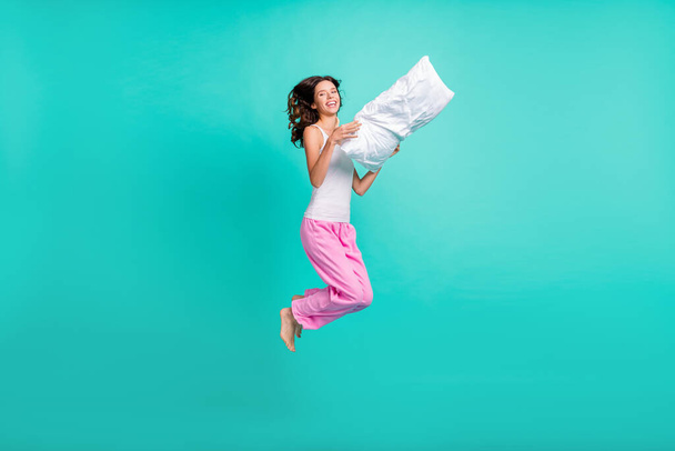 Full length photo of charming adorable young lady nightwear jumping holding pillow isolated teal color background. - Foto, Imagen